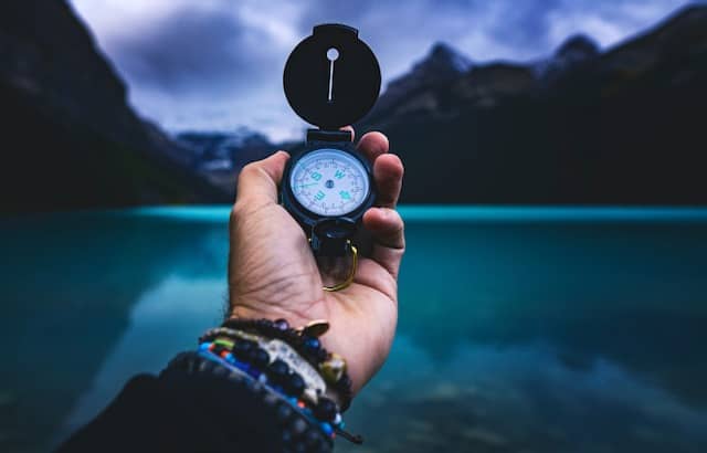 hand holding a compass in front of a mountain lake